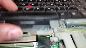 Ziehe die beiden kleinen Laschen nach oben, die zum Bildschirm ragen, um den Tastaturanschluss vom Motherboard abzuziehen.