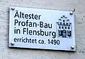 Tafel am Gebäude mit dem Hinweis auf das Alter. Die Treppe des Gebäudes hat noch eine separate Tafel, die darauf hinweist, dass sie unter Denkmalschutz steht.