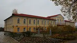Ein zweistöckiges gelbes Residenzgebäude mit großen Rundbogenfenstern im zweiten Stock und einem fast zentral angeordneten Mittelbau. Im Erdgeschoss sind die Fenster eckig.