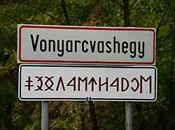 Ortstafel in lateinischer Schrift und Rovásírás