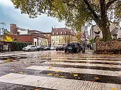 Straßenkreuzung mit Zebrastreifen. Hinten links ein flaches Ziegelgebäude der ehemaligen Werksfeuerwehr, wo perspektivisch ein Mahnmal für den Nagelbombenanschlag in der Keupstraße entstehen soll