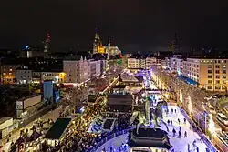 Nachtaufnahme von schräg oben auf den Kölner Heumarkt mit Weihnachtmarktbuden, bunter Beleuchtung und Eisbahn.