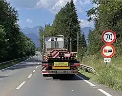 LKW Anhänger mit Stahlträgern von hinten. Am Ende der Stahlträger befindet sich eine rechteckige weiße Tafel mit rotem Rand zur Kennzeichnung als Langgutfuhr