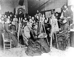 Auf dieser schwarz-weiß Fotografie sind viele Frauen, teilweise an Staffeleien sitzend zu sehen. Im Hintergrund drängen sich weitere Menschen.