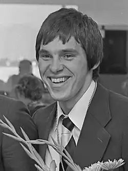 Alex Boegschoten ist auf diesem Schwarzweißfoto bei der Rückkehr von den Olympischen Spielen 1976 zu sehen. Er trägt Jacket, Hemd und Krawatte.
