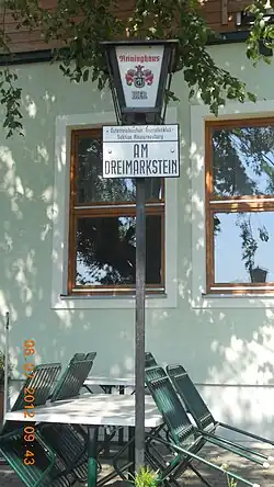 Hinweisschild beim Berggasthaus „Häuserl am Roan“, das zugleich Gipfelhütte des Dreimarksteins ist.