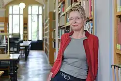Anke Berghaus-Sprengel steht an ein Bücherregal gelehnt in einem Lesesaal.
