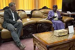 Der ehemalige deutsch Politiker Jan van Aken im Gespräch mit Ann Itto Leonardo. Ein Europäischer Mann in dunklem Anzug und eine afrikanische Frau im violetten Kostüm sitzen nebeneinander in barock anmutenden, pompösen Sesseln.
