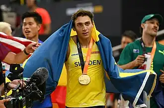 Stabhochsprungweltmeister Armand Duplantis mit Fahne über dem Kopf und umgehängter Goldmedaille