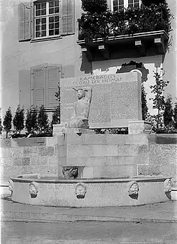 Das Wehrmannsdenkmal in seiner ursprünglichen Fassung, wo die Urne von Jakob Probst in die Mauer eingelassen ist. Zum Andenken für die im Militärdienst stehenden Grippe- und Unfalltoten aus der Basler Landschaft (Spanische Grippe-Epidemie 1918). Das Denkmal musste 1934 überarbeitet werden. Aus der Skulptur wurde ein Eichenblattzweig? herausgemeisselt und anstelle des offene Buch auf seinen Knien, ein Helm darauf gesetzt. Damit war die sakrale Symbolik des Werks zerstört.