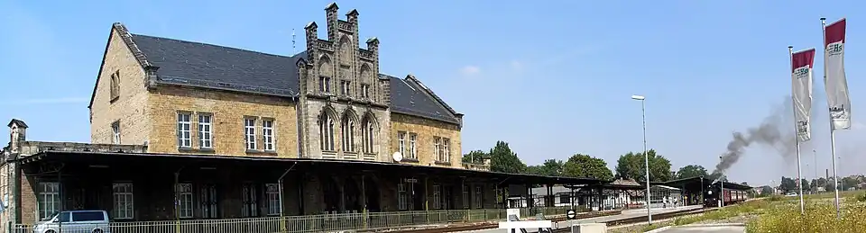 Historisches Bahnhofsgebäude in Quedlinburg mit Bahnsteig und Dampflok, die Rauch ausstößt