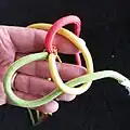 Mit dem nächsten Kardeel (gelb) geht man unter dem zuerst bewegten Kardeel (gelb) durch und unter die stehende Part des nächsten Kardeels (rot).