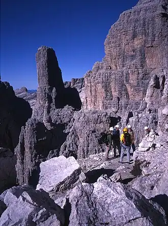 Bergsteigergruppe auf dem Sentiero delle Bocchette Centrali, im Hintergrund die Ostwand der Guglia (Campanile Basso)