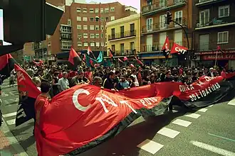 Eine Gruppe von Menschen zieht mit Flaggen und einem Banner der CNT durch eine Straße.