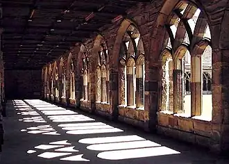 Seitliche Farbfotografie von einem Kreuzgang mit Blick in den Innenhof. Durch die mittelalterlichen Rundbögen fällt das Tageslicht auf den Boden. Die dunkle Decke ist kaum zu erkennen.