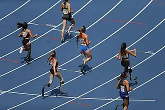 Die blauen Bahnen des Stadions erstrecken sich gleichmäßig, während die Läuferinnen in verschiedenen Formationen auf der Strecke unterwegs sind.