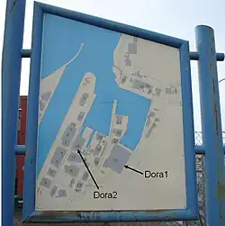 Schild mit Gebäuden im Hafengebiet des Fjords mit Pfeilen, die auf die Dora-Komplexe hinweisen.
