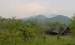 Eine grüne Landschaft mit Bergen im Hintergrund und einem Haus auf der rechten Seite.