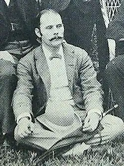 Edward John Cameron, 1885. Schwarz-Weiß-Bild von einem Mann mit dünnem Schnurrbart im Schneidersitz.