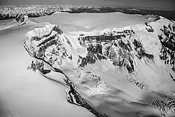 Der flache Gipfel eines schneebedeckten Berges mit einem felsigen und schneebedeckten Steilhang im Vordergrund