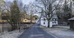 In der Mitte ist eine Straße, rechts ein Haus, links ein Teich