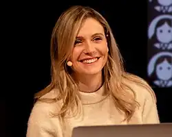 Elizabeth Pich während einer Lesung an einem Tisch, Laptop steht vor ihr, sie lacht