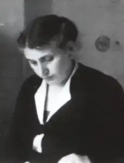 Schwarz-Weiß-Porträtfotografie von Ella Kroch, eine Frau mit einer für die Zeit typischen Frisur und dunkler Kleidung, nach unten schauend