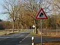 Straße mit durch Bäume eingeschränktem Lichtraumprofil und aktuellem Verkehrszeichen