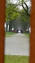 Blick durch einen schmalen Spalt von der Stelle des ehemaligen Haupttors auf die ehemaligen Lagerstraße
