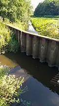Im Vordergrund die Boholzer Au und hinter der Trennmauer die Oxbek am Kreuzau-Bauwerk im FFH-Gebiet