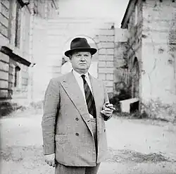 Hüftbild, schwarzweiß, aus dem Jahr 1959, von Waugh mit Hut und Zigarre vor Ruine