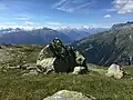 Die Fotografie zeigt einen Hügel der Fiescheralp (Schweiz) mit Wiese und Felsen im Vordergrund. Dieser dient als Repoussoir und unterstreicht die Weite der Landschaft.
