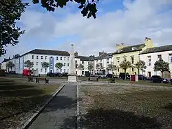 Dieses Farbfoto zeigt in einer etwas entfernten Frontaufnahme dem Fleming Square mit dem mittig auf dem Platz befindlichen Denkmal und den dahinter stehenden Häusern. Es wurde 2007 aufgenommen.,
