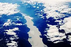 Luftbild eines schmalen Fjords in einer gebirgigen Landschaft. Im Bild sind viele Wolken und eine Gletscherfläche zu sehen.