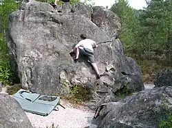 Kind an einem Felsblock, ca. 4&nbsp;m hoch, mit einer Matte darunter