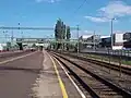 ein langer Mittelbahnsteig an einer elektrifizierten Bahnstrecke, über den eine Fußgängerbrücke führt
