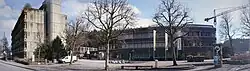 Aus Beton erbautes Schulhaus, bestehend aus zwei Gebäudelementen mit Vorplatz.