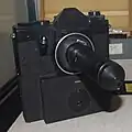 Kamera mit Sonderobjektiv SO-3.5.1 zum konspirativen Fotografieren. Das Objektiv konnte auf eine geräuscharme Spiegelreflexkamera geschraubt werden. Damit war es möglich, durch ein Loch von 1&nbsp;mm Durchmesser zu fotografieren.[171]