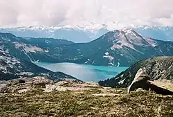 Ein symmetrischer Berg erhebt sich über einen türkisfarbenen See im Vordergrund; im Hintergrund vergletscherte Berge