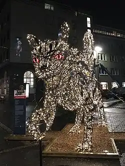 Das Foto zeigt eine übermenschengroße, von innen beleuchtete Skulptur einer Katze mit erhobener rechter Pfote, ausgestreckten Krallen, geöffnetem zahnbewehrten Maul und roten Augen.