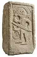 Die Grabstele von Niederdollendorf zeigt einen Krieger. Dieser hält mit der einen Hand ein Schwert und mit der anderen kämmet er sich mit einem Kamm die Haare.