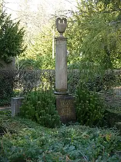 Grab mit goldener Inschrift auf dem Sockel einer runden Marmorsäule, die von einer Urne überragt wird