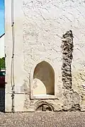 Prangerstein links am Portal – wegen der Aufschüttung der Stadt ist nur noch die Spitze (Kopf mit Zipfelmütze als Spottfigur) zu sehen