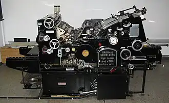 Rechts oben sieht man den Anlagestapel mit dem Sauggreifer, der den Bogen in Einzelanlage über den gewölbten Anlegetisch in die Maschine führt.