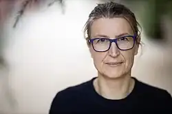 Porträt von Heike Baranowsky, im Hintergrund verschwommen ein Parkweg, Pflanzen, über ihr Zweige