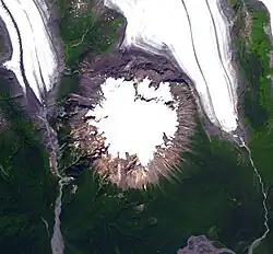Draufsicht auf einen kreisförmigen, eisbedeckten Berg mit zwei südwärts strömenden Gletschern im Nordwesten und Nordosten