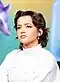 Isabela Merced auf der SXSW 2025. Sie hat mittellanges, welliges, dunkelbraunes Haar, das locker gestylt ist. Sie trägt einen weißen Rollkragenpullover, der elegant und schlicht wirkt, sowie silberne Ohrringe. Der Hintergrund ist unscharf und zeigt eine grüne und gelbe Farbgebung.