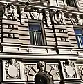 Farbige Nahaufnahme eines Fassadenteils mit Kopfreliefs zwischen den Fenstern und einem Tierkopf über dem Torbogen.