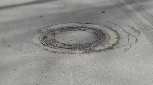 Risse durch Straßenhebung um einen Kanaldeckel