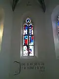 Zentrales Kirchenfenster, darunter Wandinschrift auf Sursilvan: "Jesus sagt: Ich bin der Weg, die Wahrheit und das Leben"